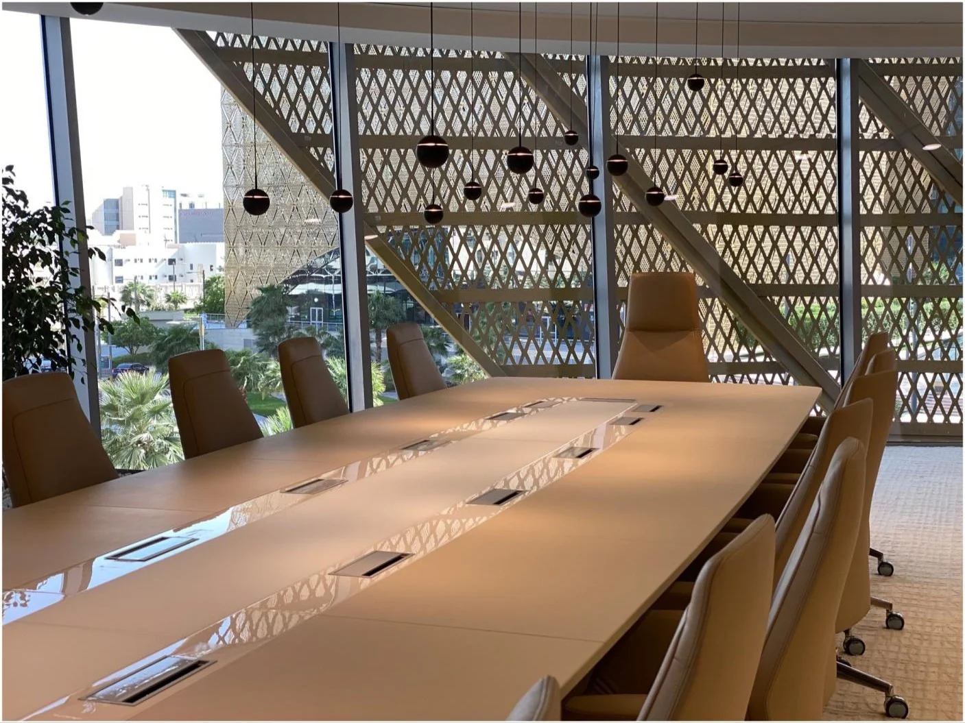 Long timber meeting table beside a patterned facade screen.