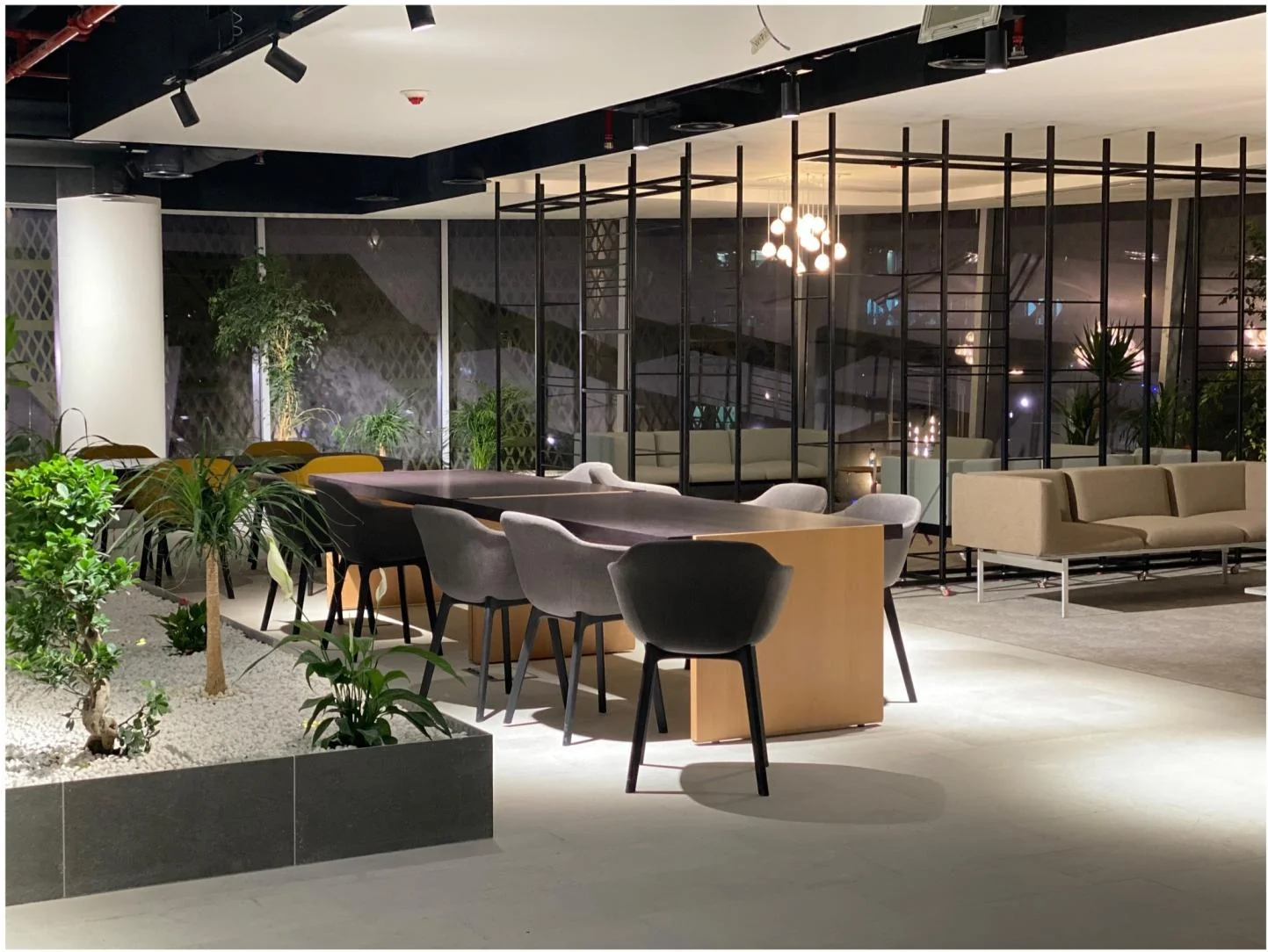 Shared lounge with planted dividers, high tables and pendant lighting.